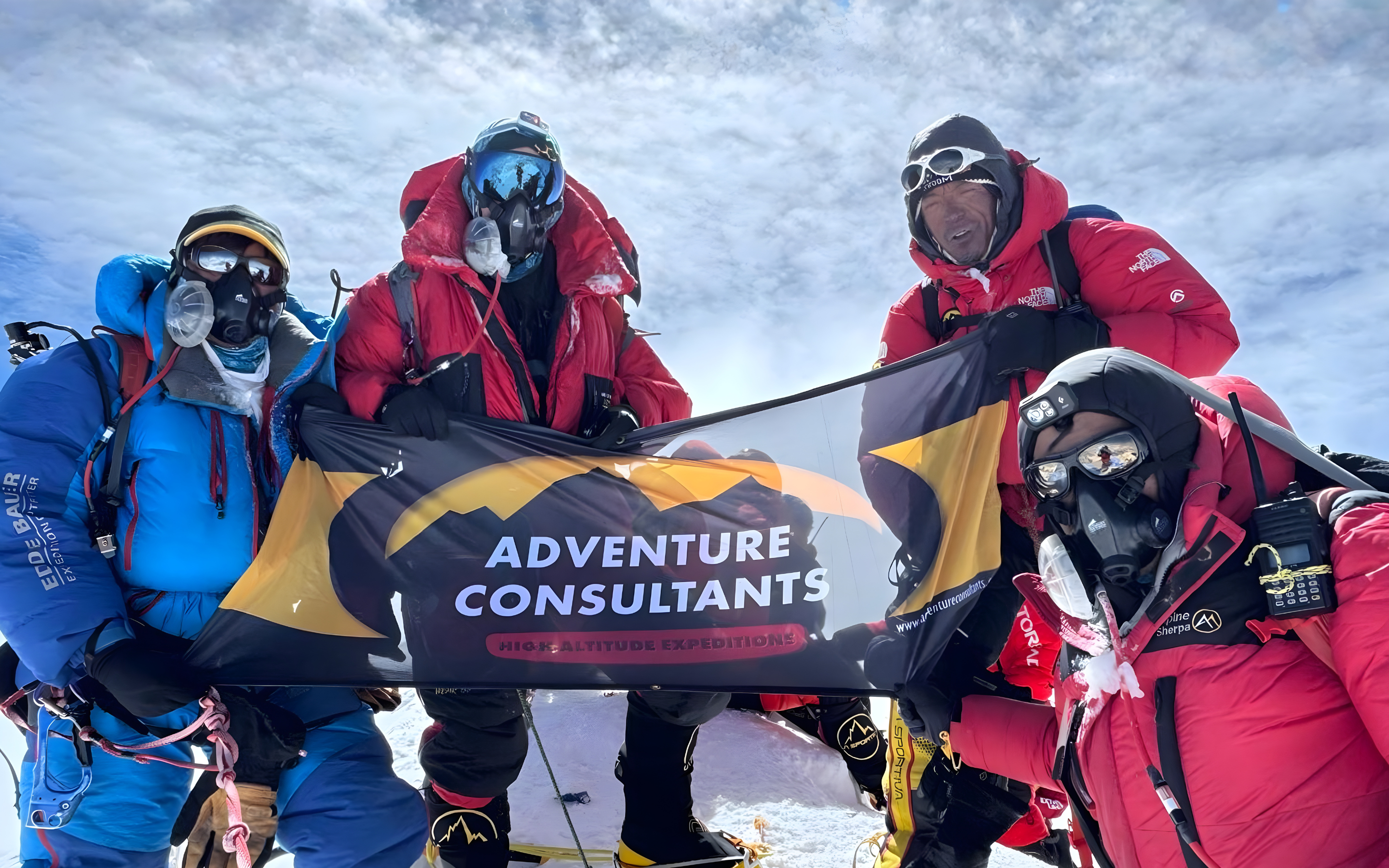 High-altitude mountaineers on Mt Everest summit holding an Adventure Consultants banner, showcasing guided expeditions, safety focus.