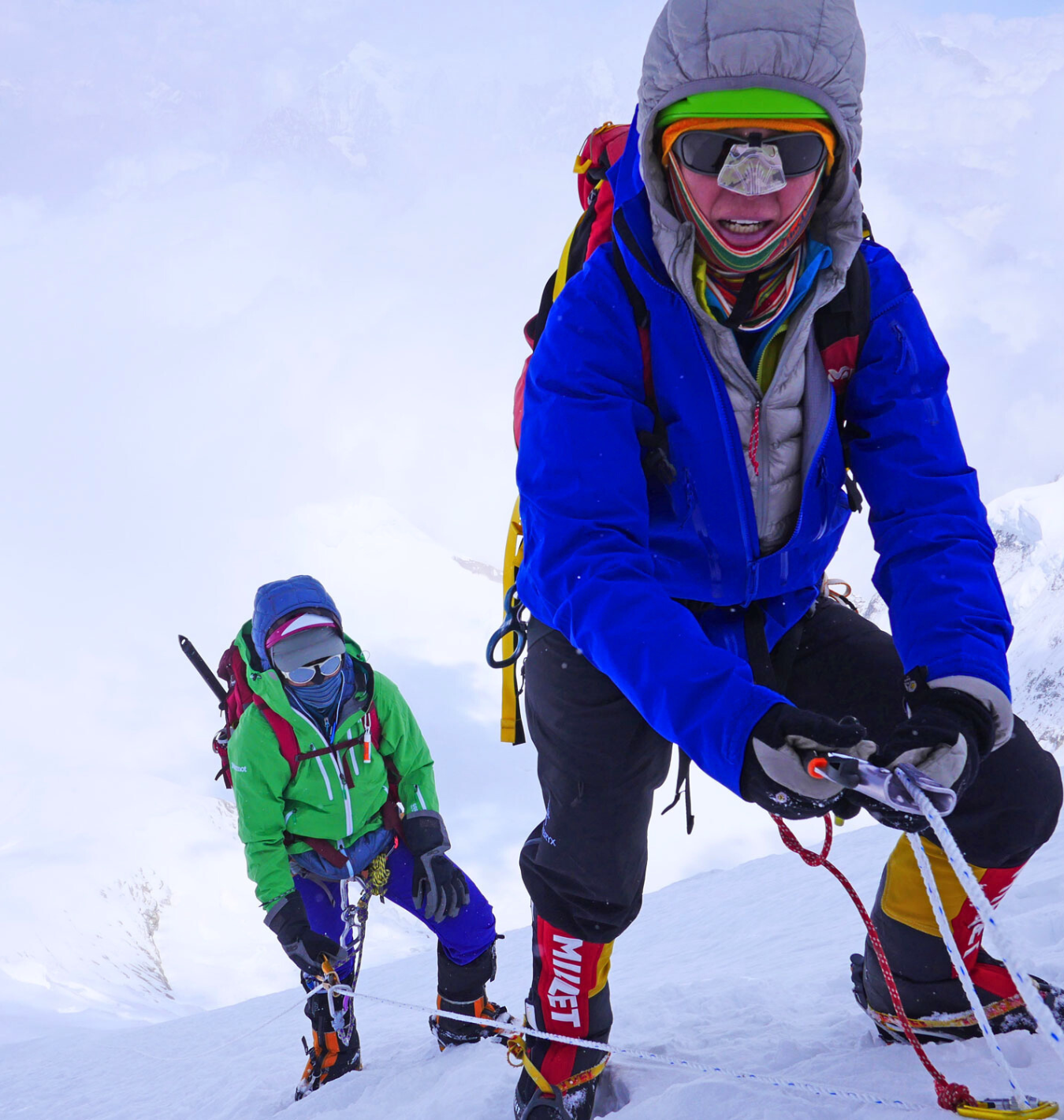High-altitude climbers ascending a steep snowy slope, roped together with ice tools, demonstrating teamwork and technical mountaineering skills.