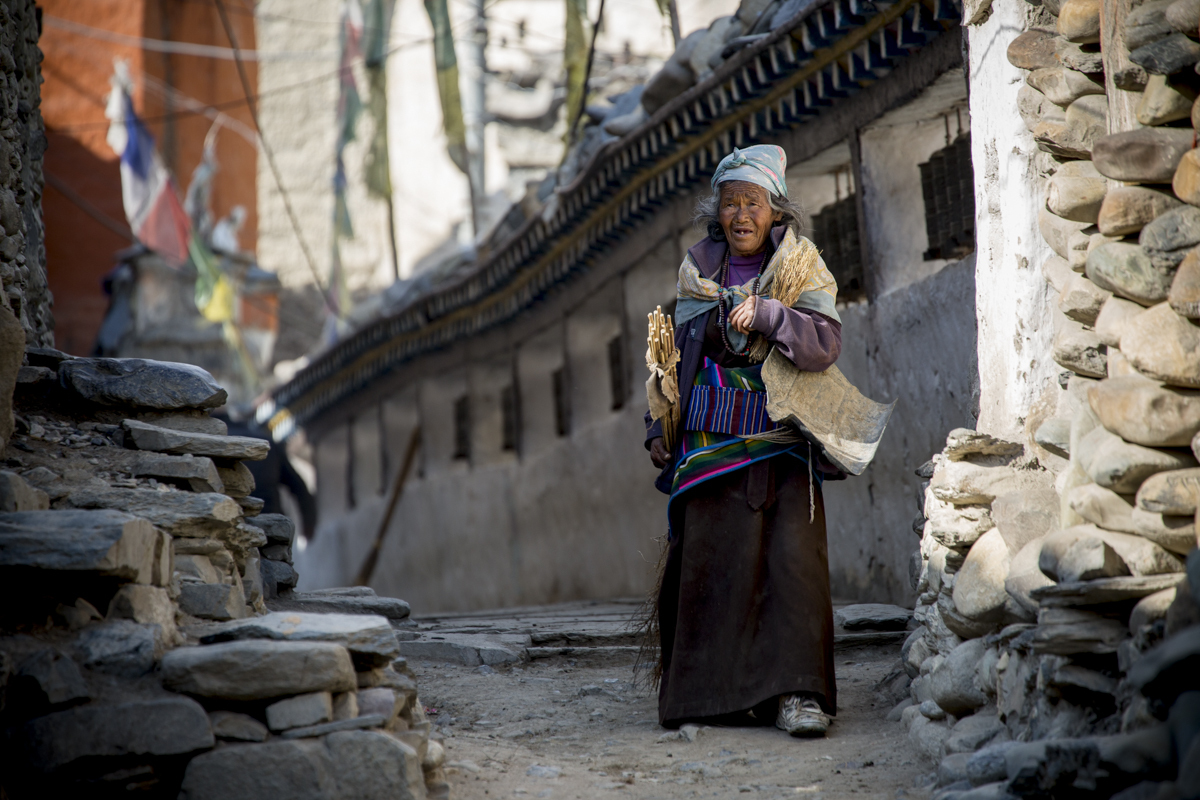 An elderly local woman carries supplies through the paved streets of Kagbeni.