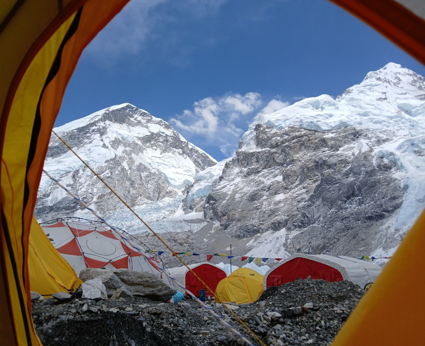 A view through a tent door across the Adventure Consultants Everest Base Camp with red, white and yellow tents on the glacial moraine and Nuptse, the Khumbu Icefall and the west shoulder of Everest behind.