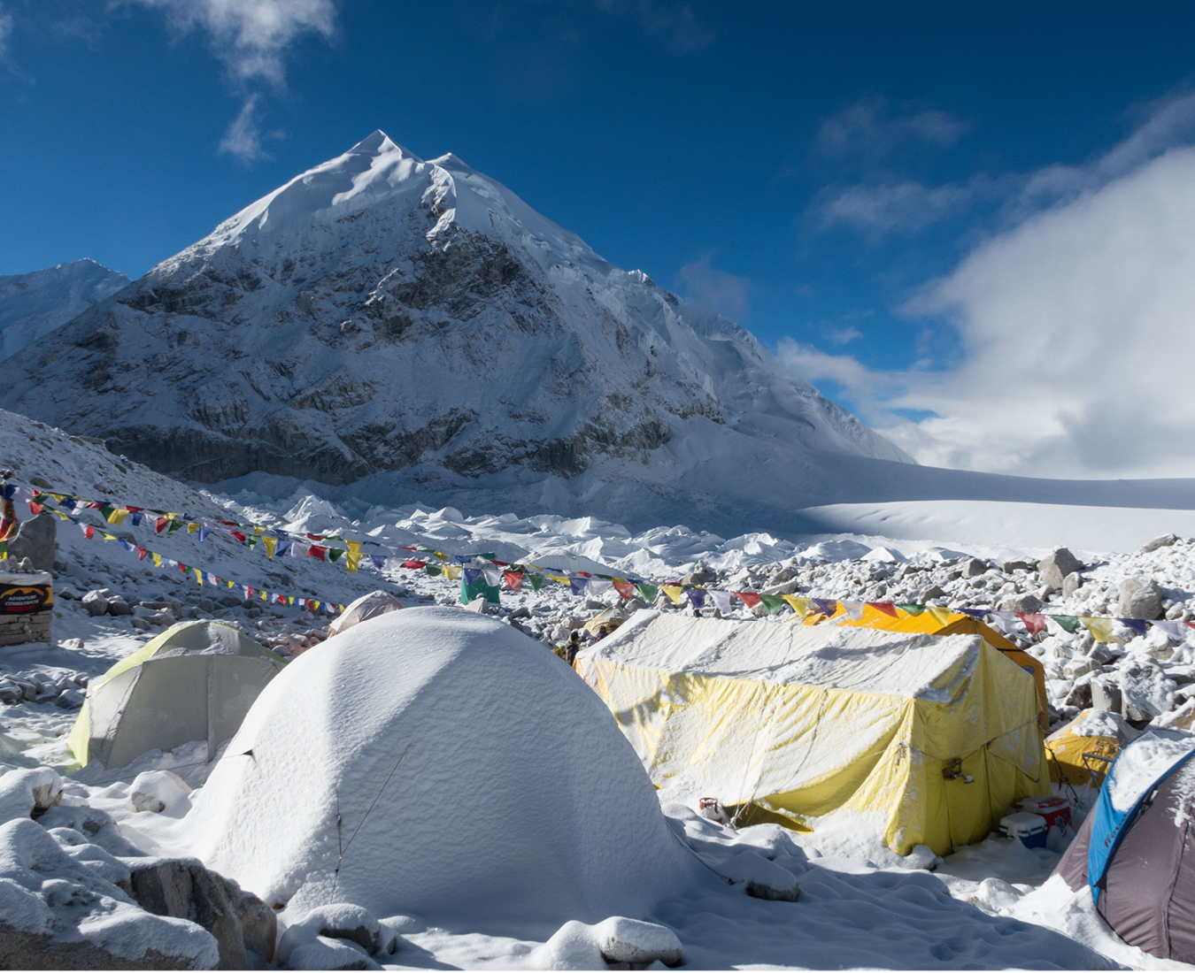 Fresh snow covers tents at Cho Oyu Base Camp, the world's 6th highest mountain Cho Oyu in the distance and prayer flags wave in the breeze.