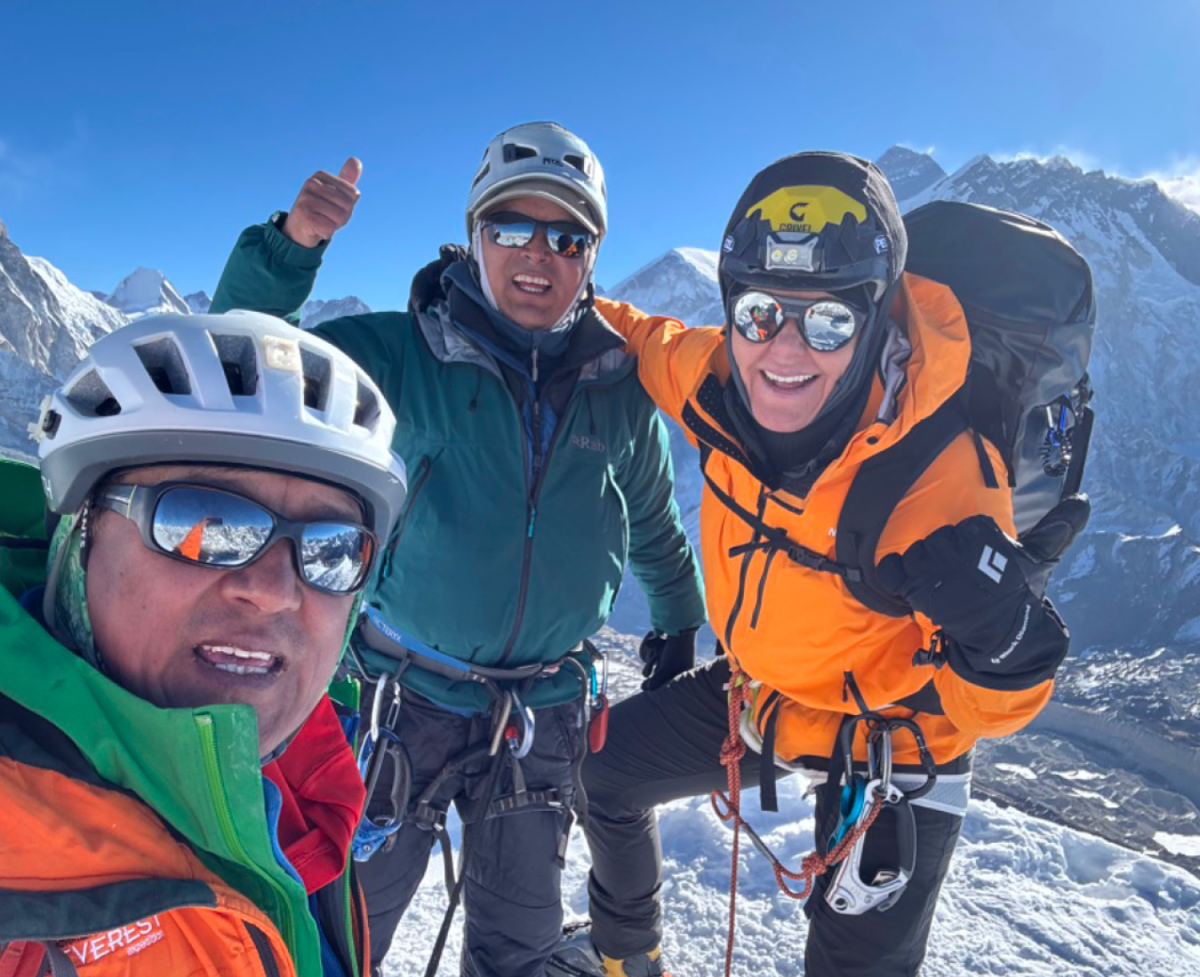 AC Guide Ang Dorjee Sherpa captures his team on the summit of Lobuche East with perfect conditions, blue sky and a view of Mount Everest behind them. All three have big smiles and thumbs up!