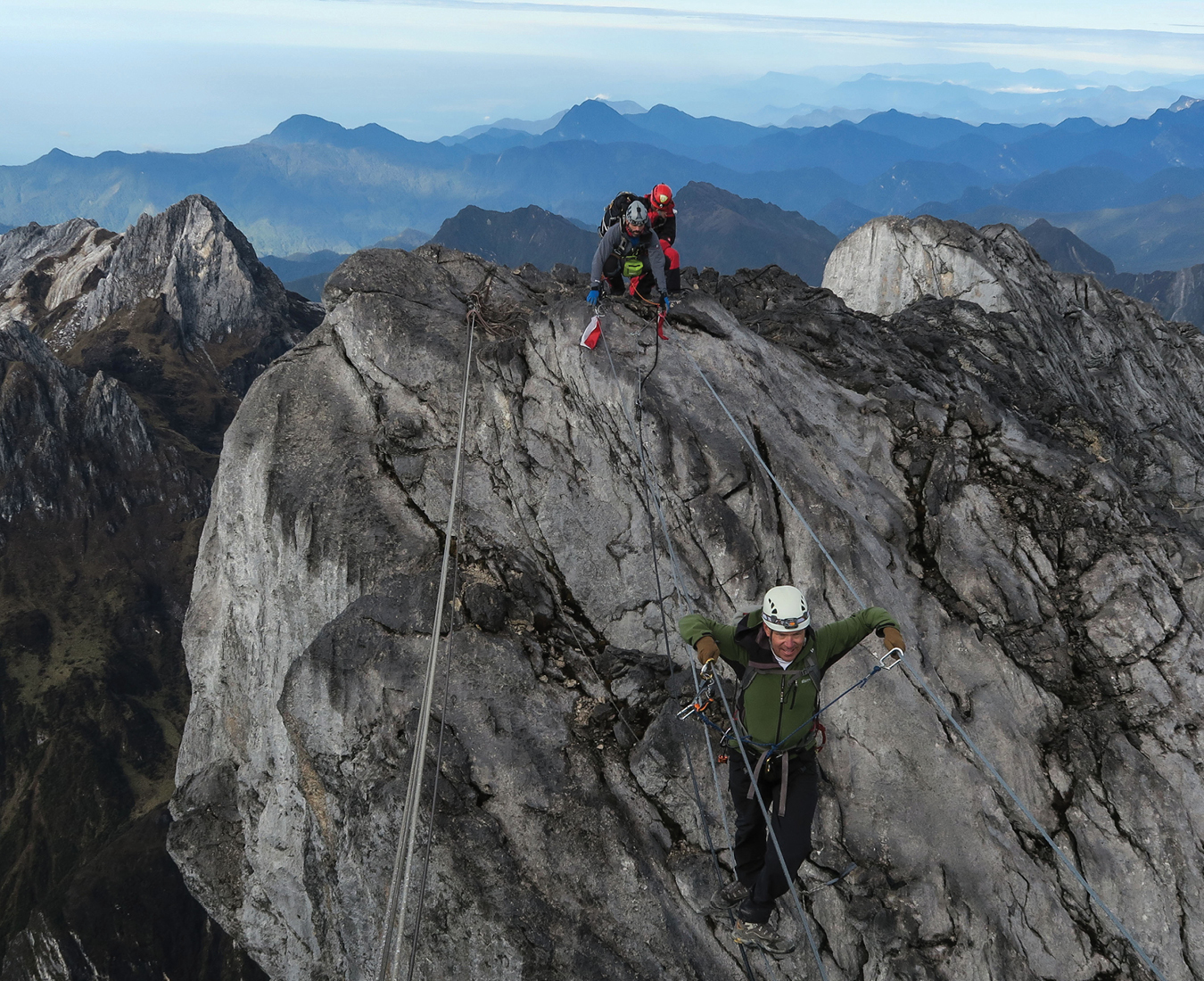 A climber crosses the infamous three-wire bridge close to the summit of Carstensz Pyramid, the remote  Western Papua wilderness stretching out across the horizon.