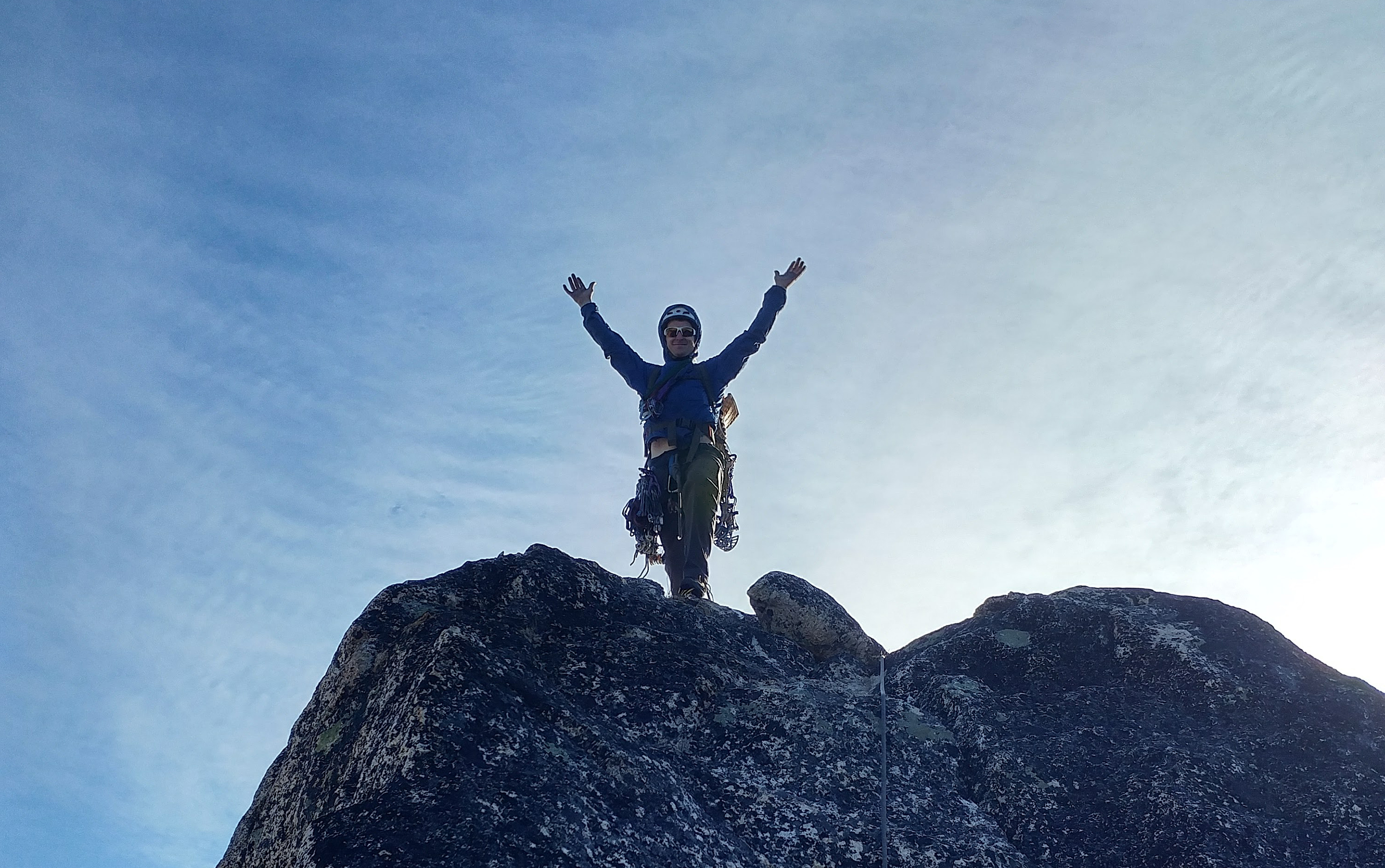 A climber celebrates, arms outstretched at the top of a rock climb.