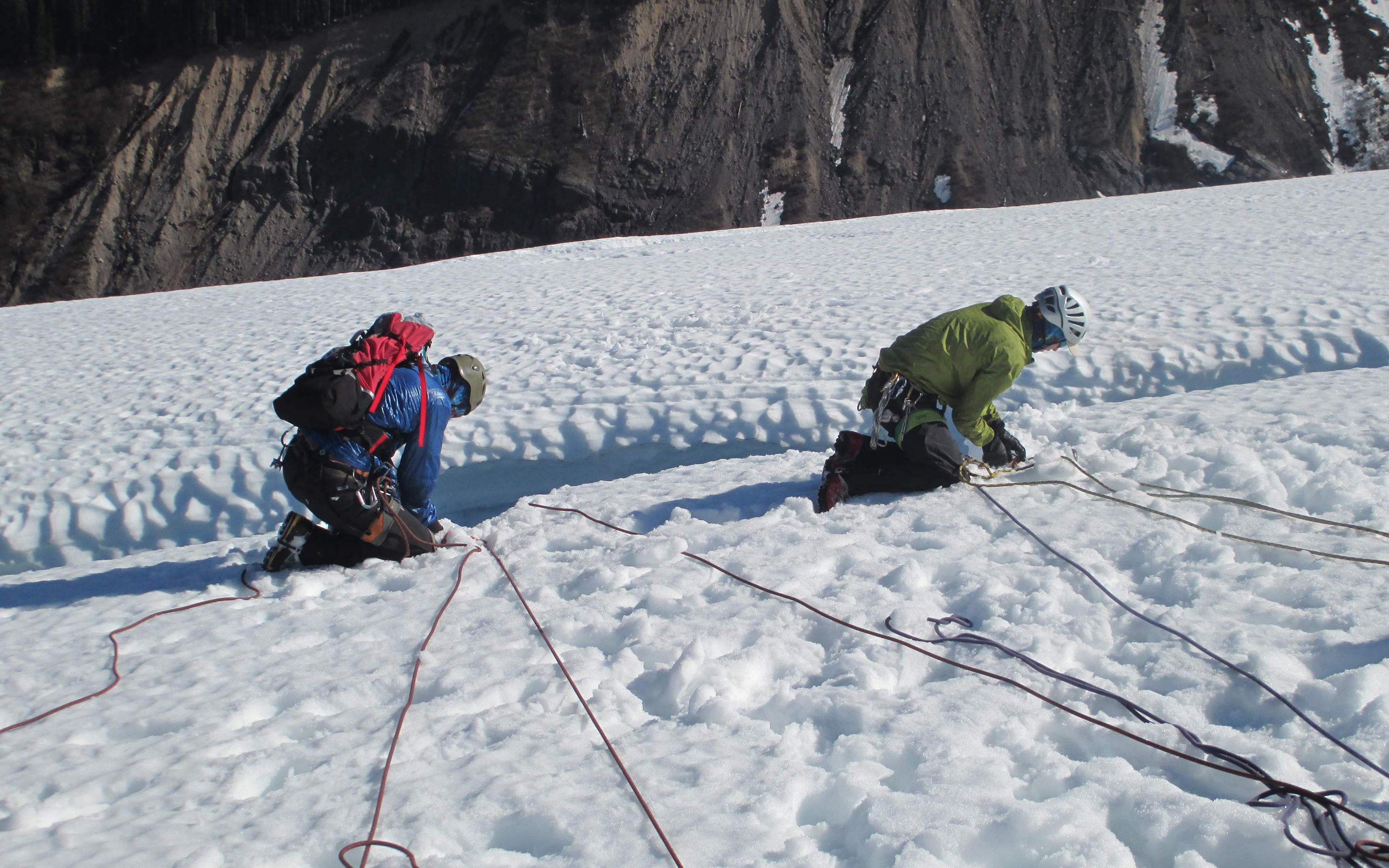 Two climbers at the edge of a crevasse setting up rescue systems on the Alpinism 1 course.
