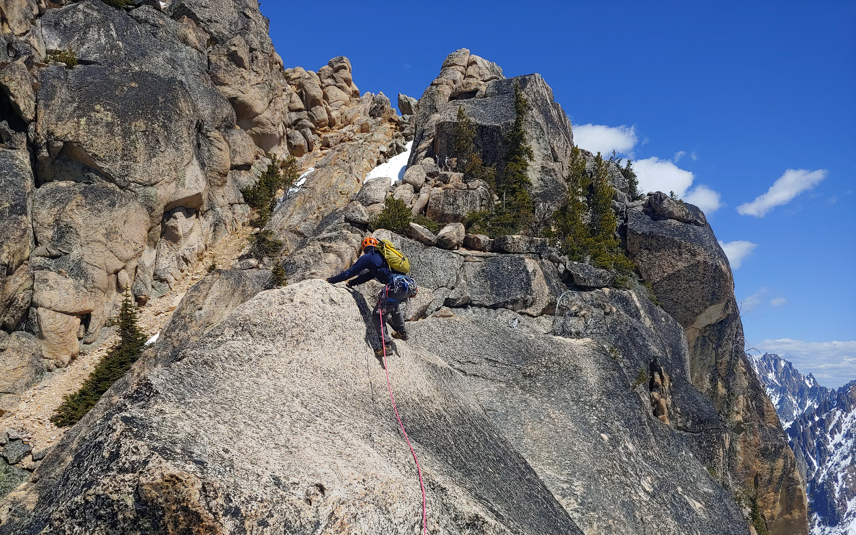 A climber approaches the top of a alpine rock pitch with huge rock pillars above