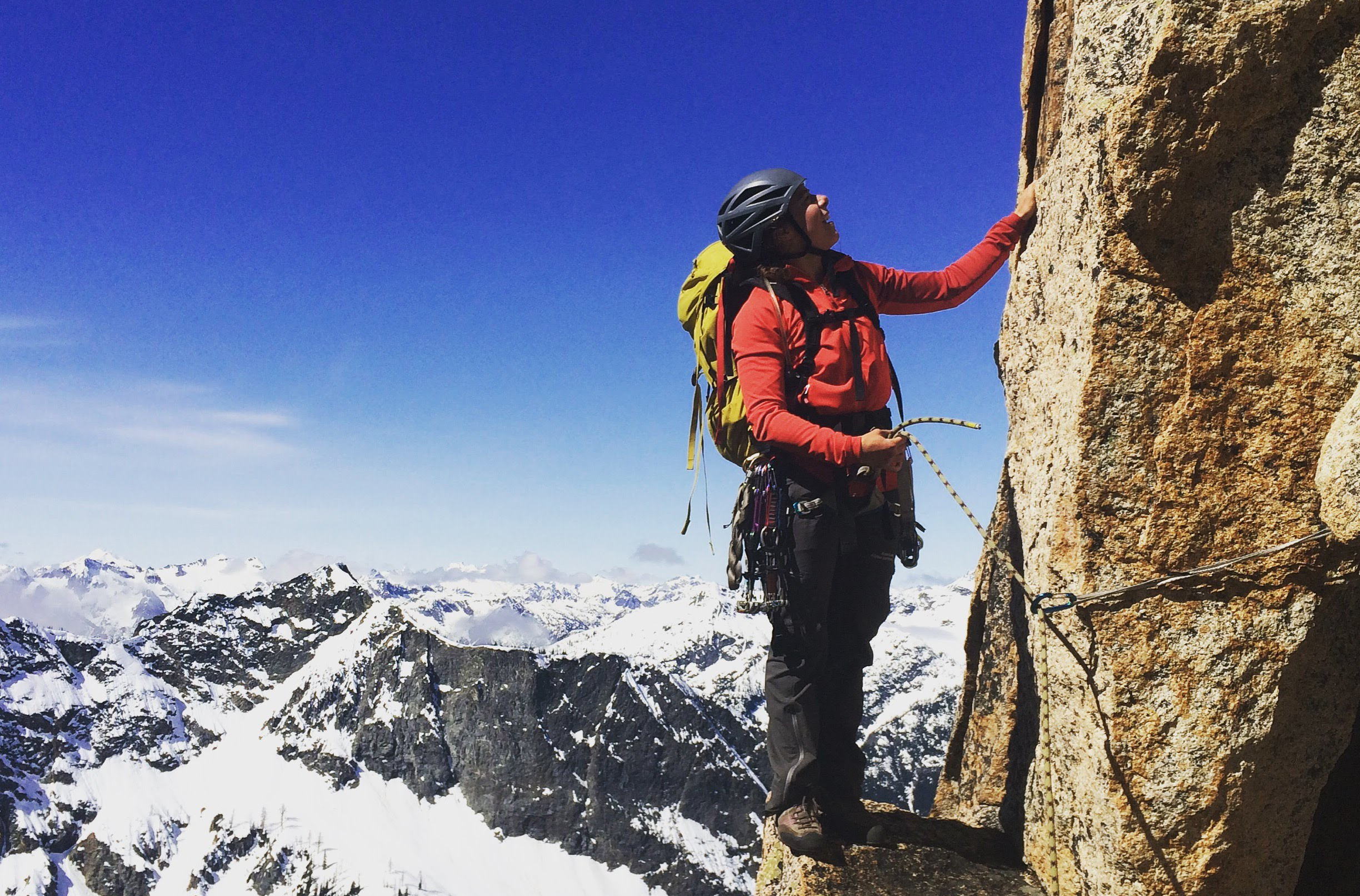 A climber pauses on a ledge to check out the route above on classic alpine rock route Beckey, Liberty Bell, Washington