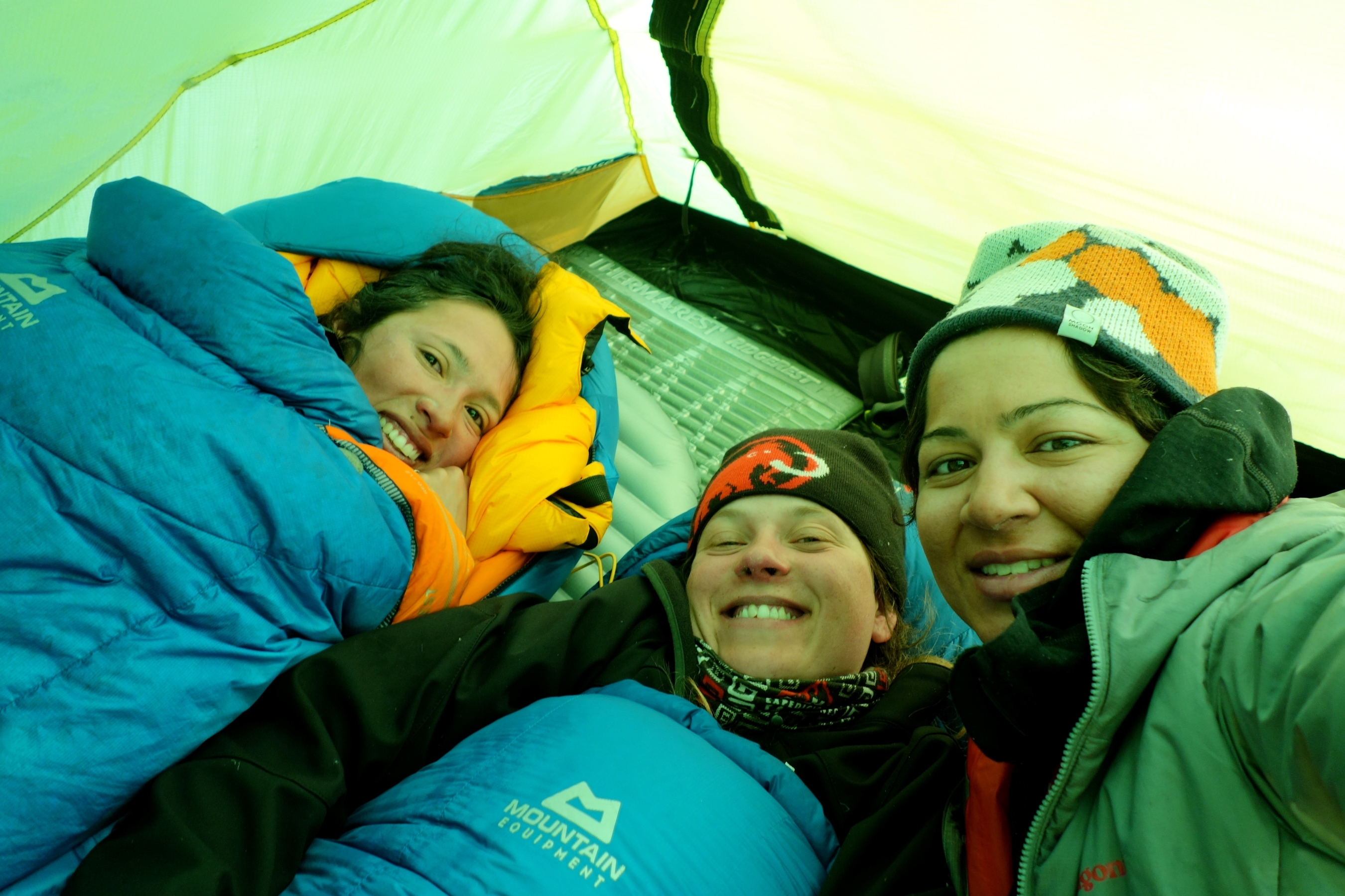 Climbers snuggle into their sleeping bags on expedition inside their tent.