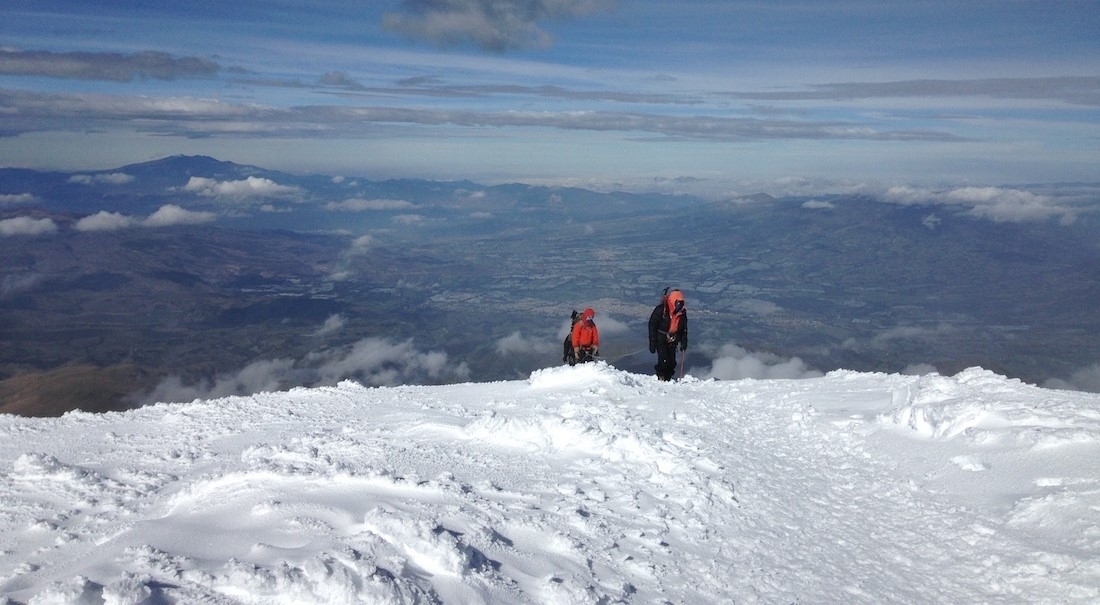 Two climbers make their way up a snow slope, the open expanse of Ecuador below.