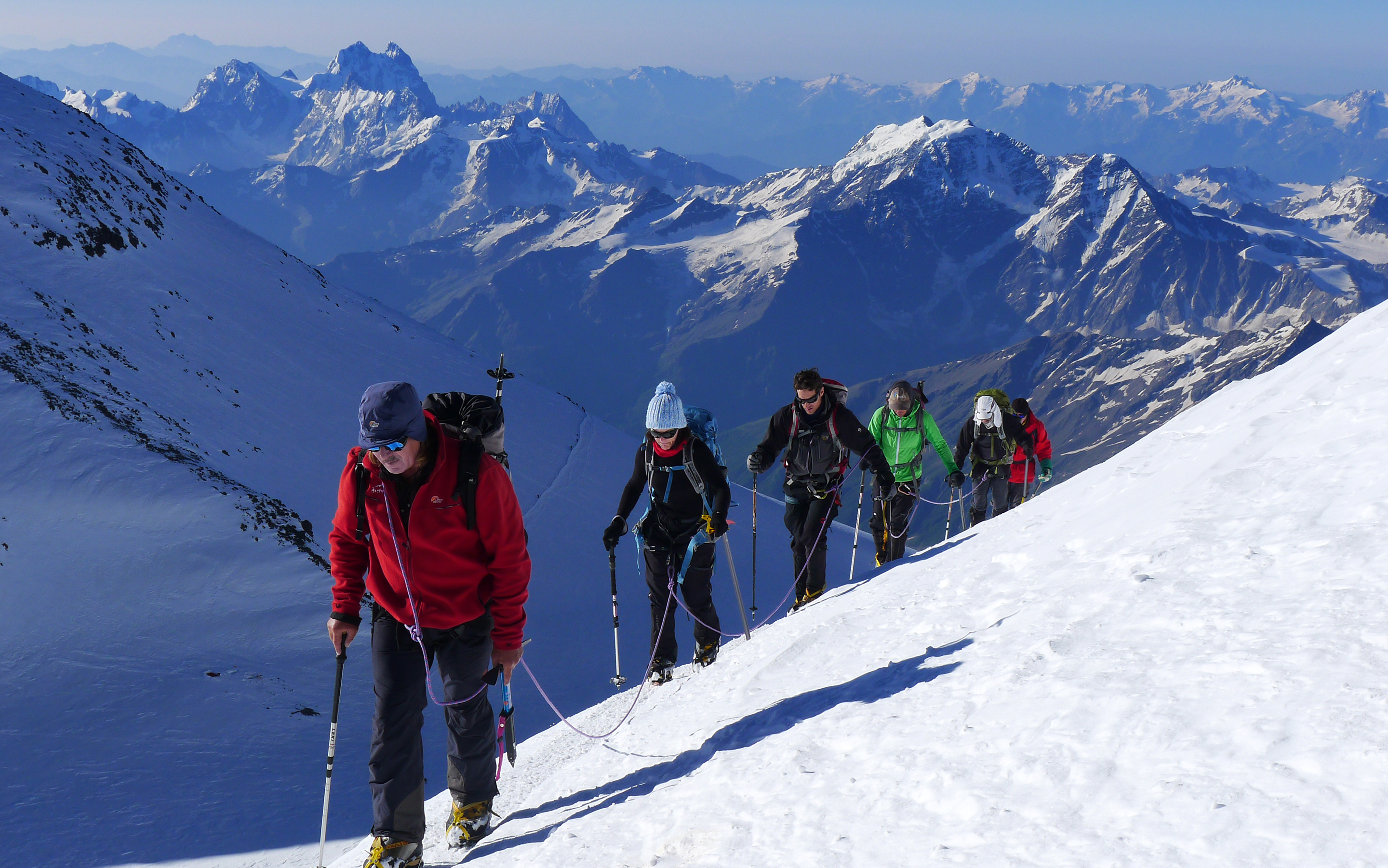 A team climb up towards the summit of Elbrus with the Caucasus mountains stretching out in the distance.